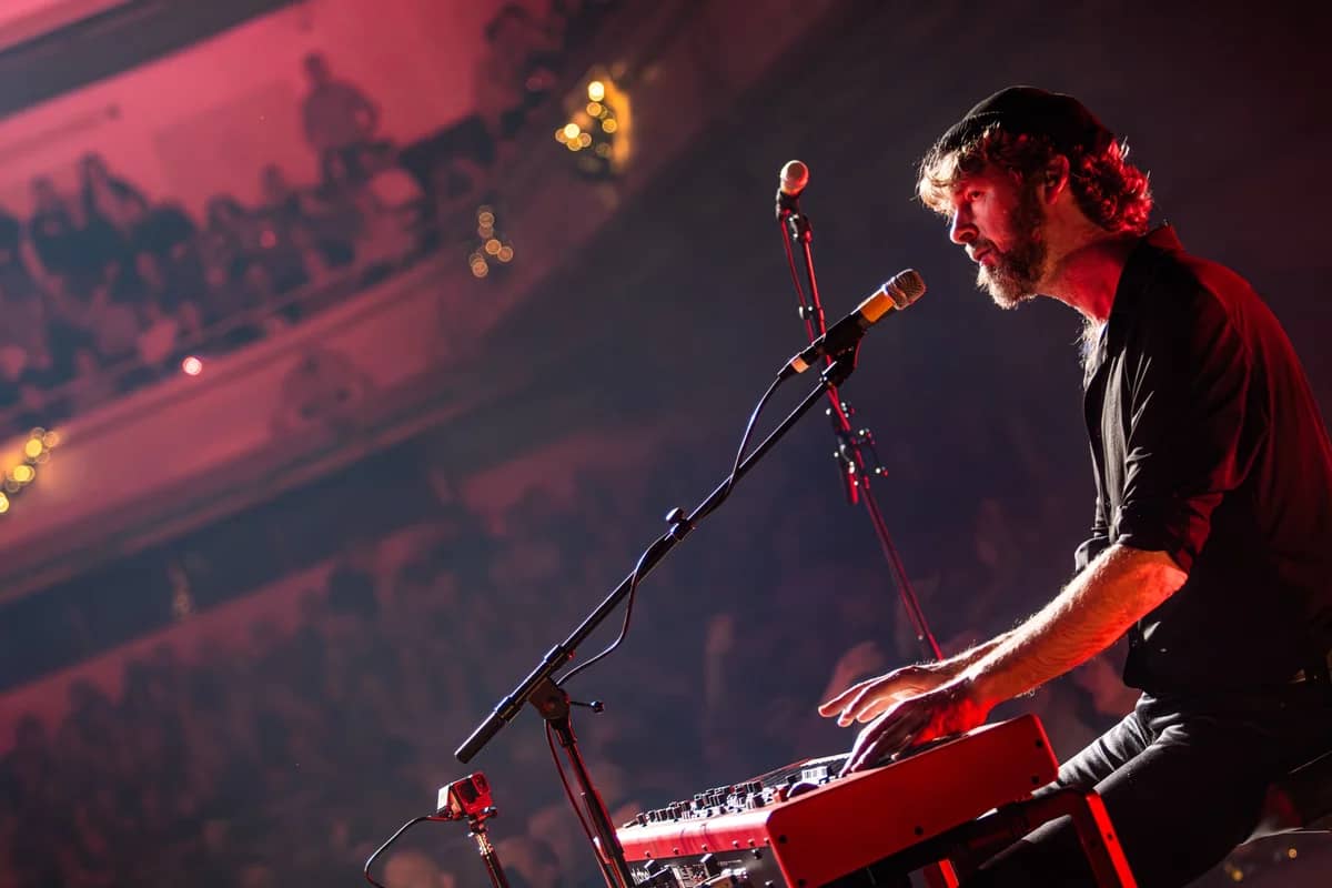 Toetsenist bespeelt zijn Nord Stage keyboard voor een volle theaterzaal met balkon, rode en warme podiumverlichting