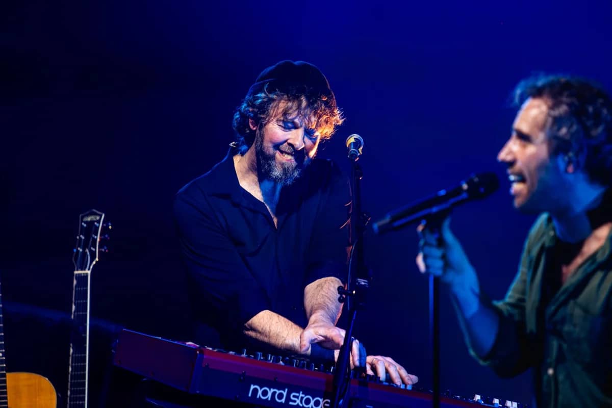 Close-up van toetsenist en zanger die samen optreden, Nord Stage keyboard en akoestische gitaar zichtbaar in blauw licht